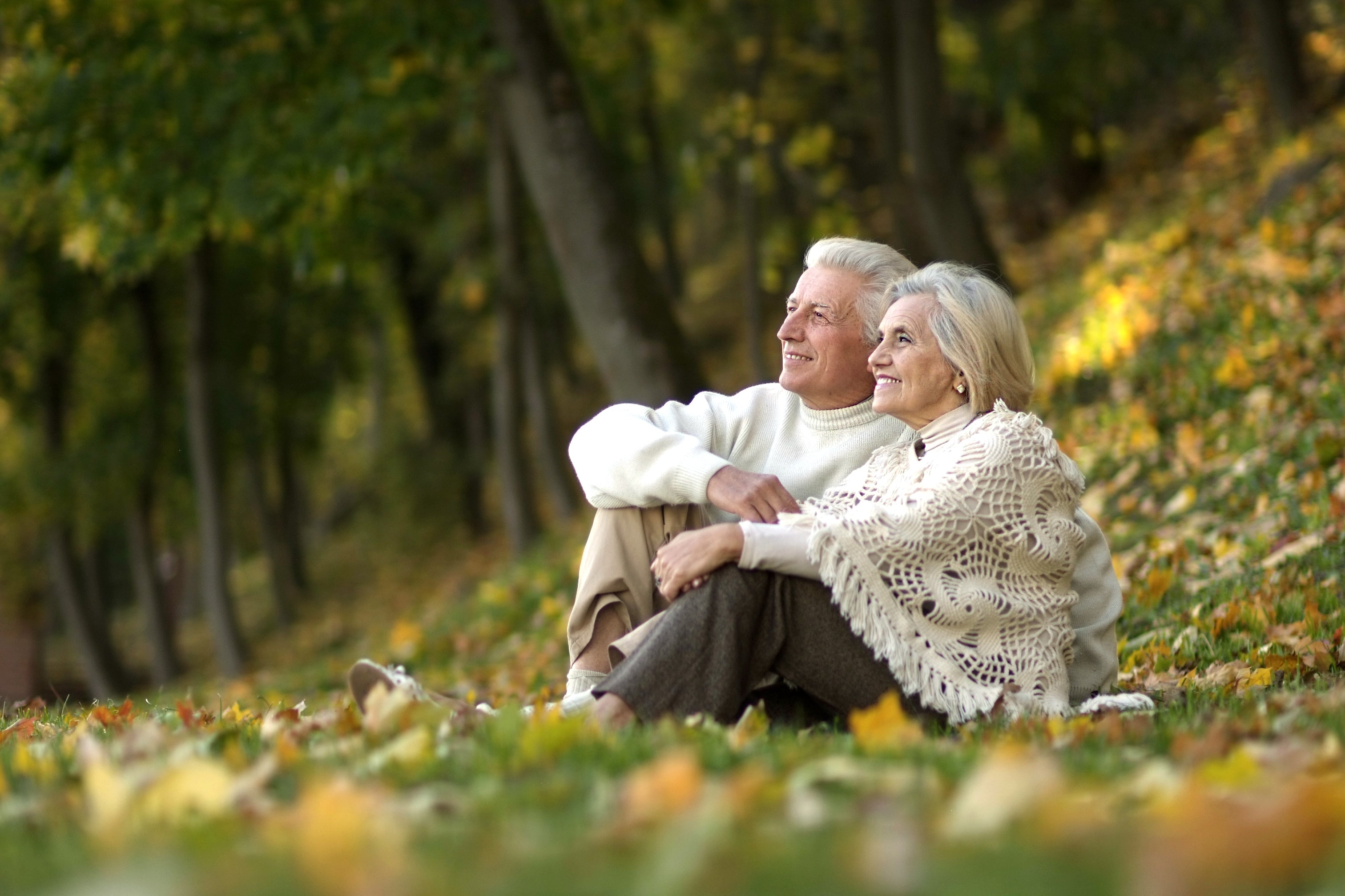 Man en vrouw samen zittend in een veld voor een bos